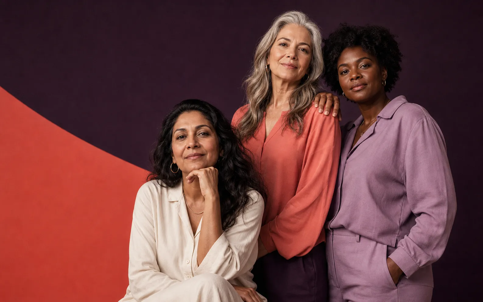 Three adult women of different generations standing together in a bold aubergine and coral editorial portrait